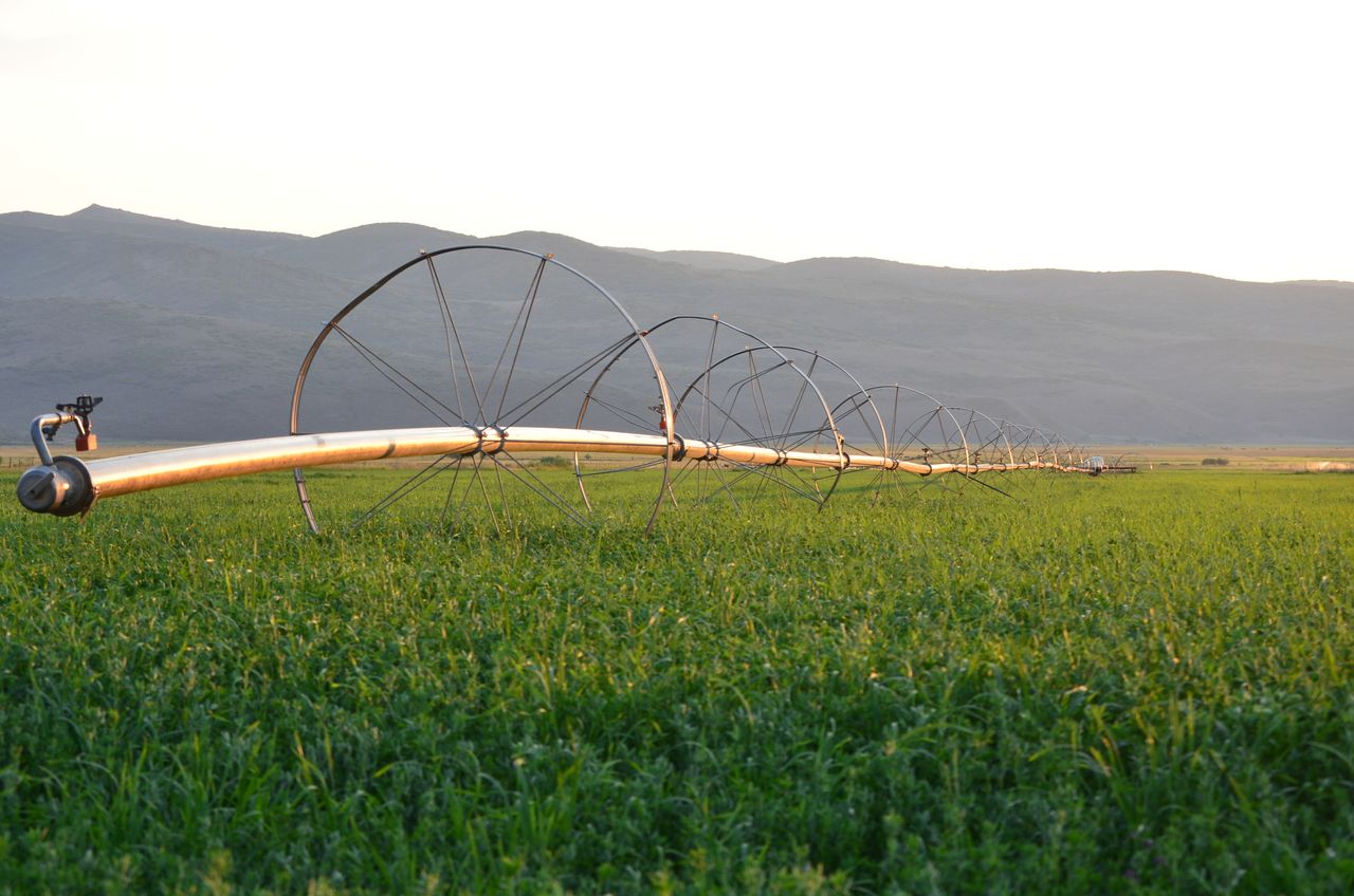 Center-pivot irrigation system extending across a green farm field with mountains in the background