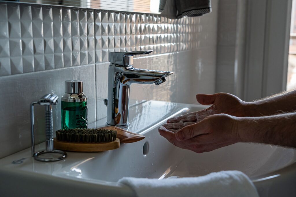 A modern bathroom sink with lathered hands under a faucet