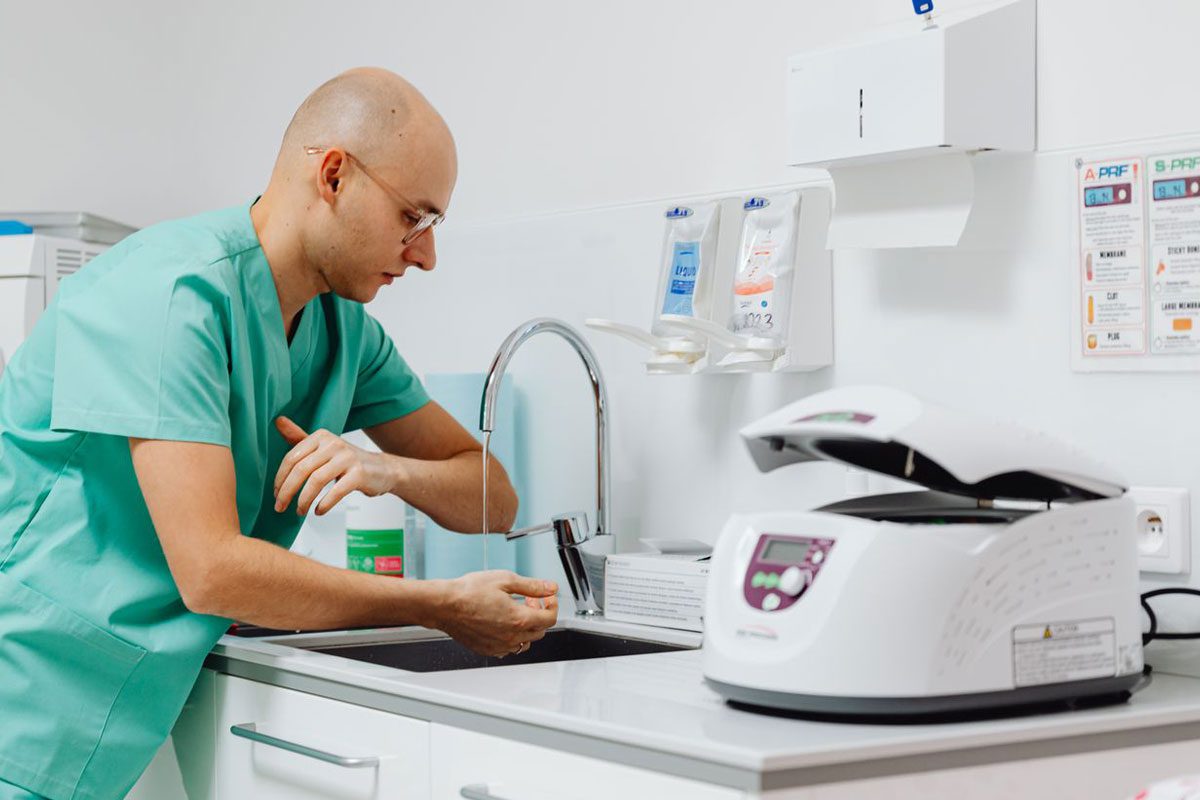 Person in green scrubs washing their hands at a sink beside medical equipment